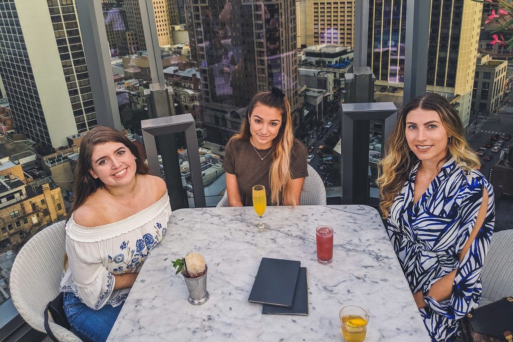 3 girls sit with drinks surrounded by Chicago skyscrapers 