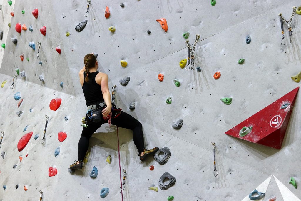 man on rock climbing wall, holding on with 1 hand