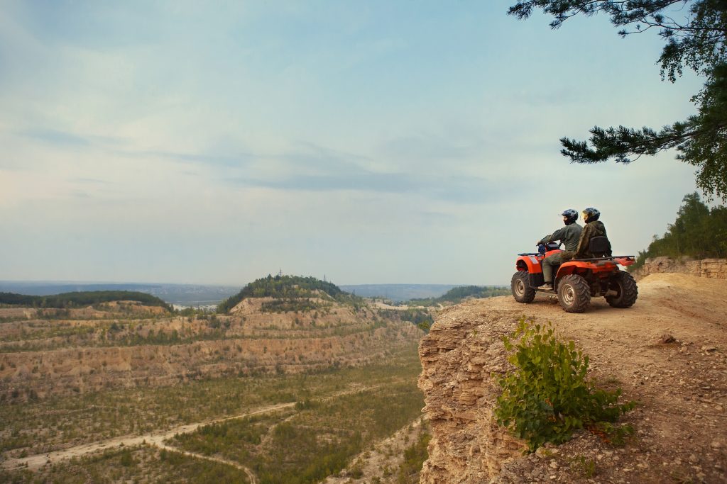 Beautiful couple is watching the sunset from the mountain sitting on ATV