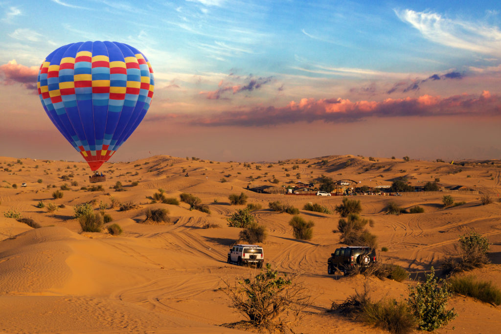 Hot air balloons landing sky in a desert sand dune is a popular activity rally off-road car among tourists in Dubai.