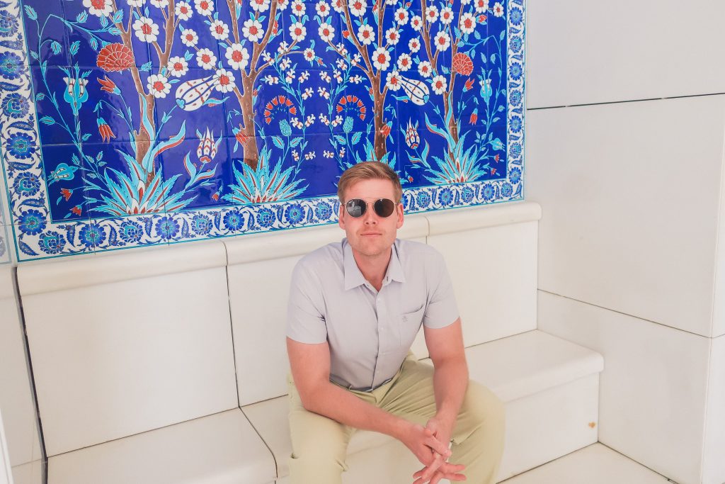 man sitting in front of beautiful tile design at Sheikh Zayed Grand Mosque