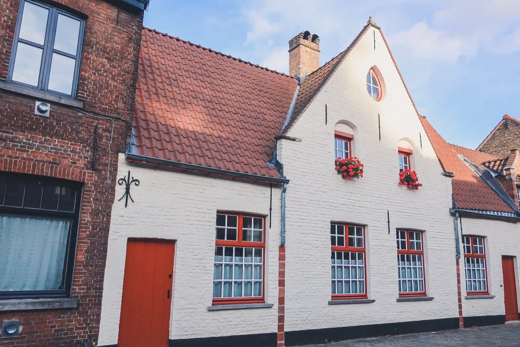 Home in Bruge with white paint and red door, red trim and red flowers