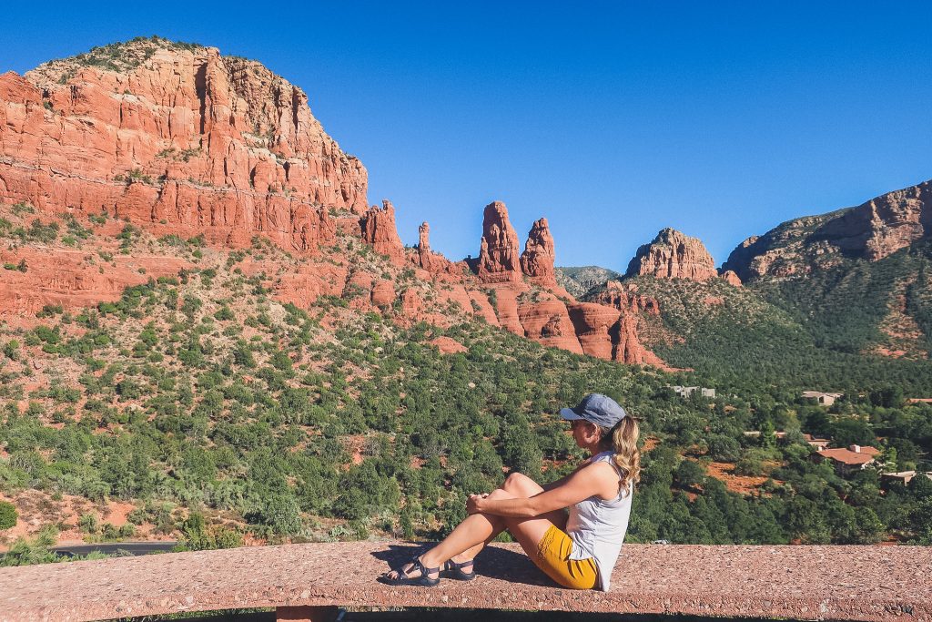 Girl sits on ledge and looks at Sedona Red Rocks from Chapel of the Holy Cross