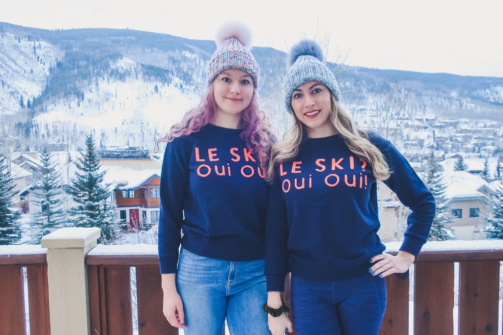 two girls wear fur pom knit hats and logo tees that say " le ski, oui oui"