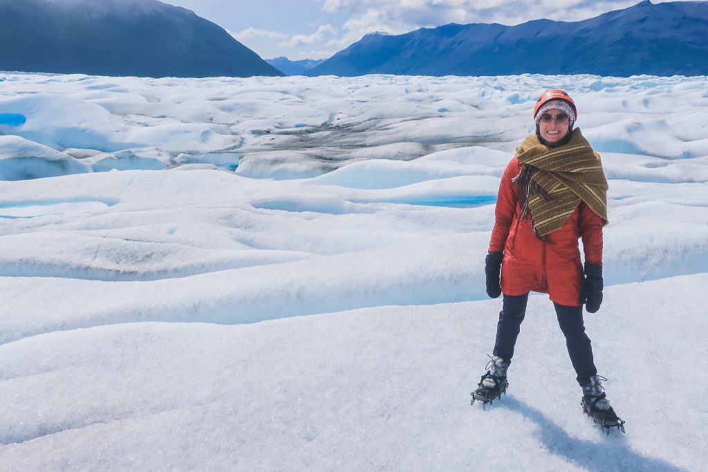 woman stands on glacier wearing compressible jacket and wool blanket scarf