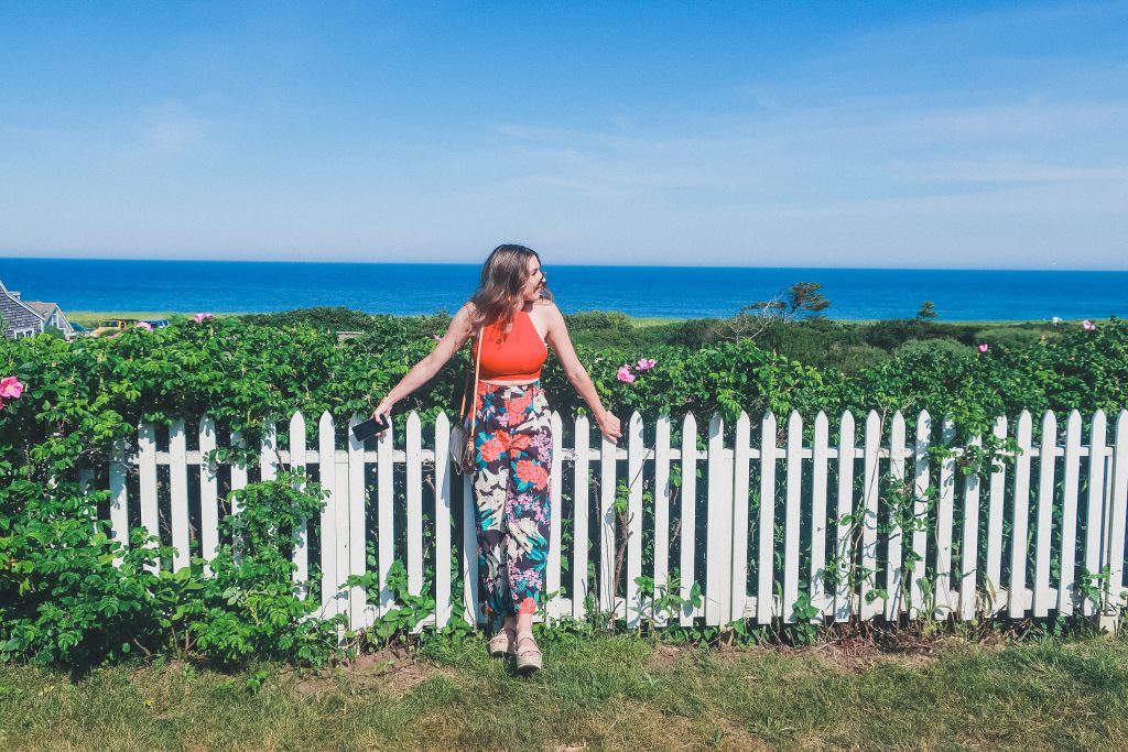 woman relaxes next to white picket fence near Sconset Bluff Walk on Nantucket