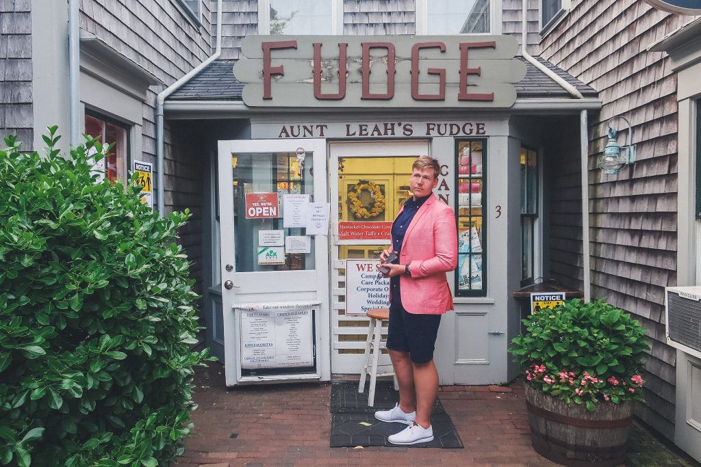 man stands outside aunt Leah's Fudge shop in Nantucket around sunset