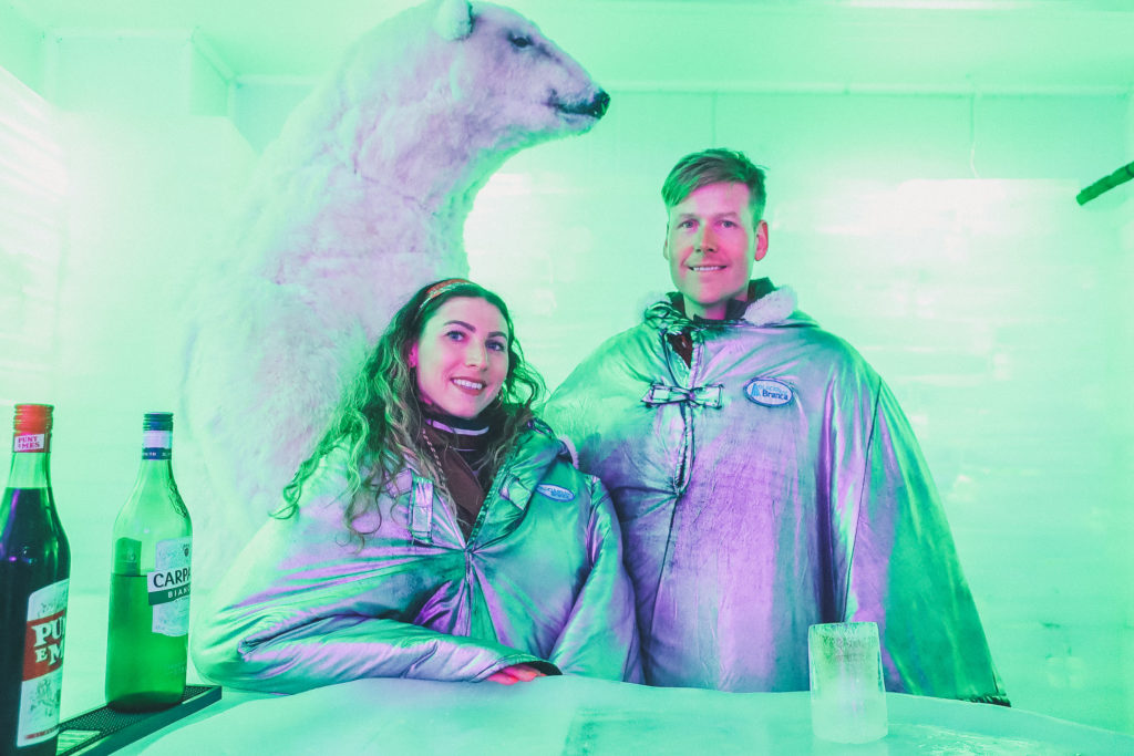 couple stands next to polar bear at ice bar in el calafate