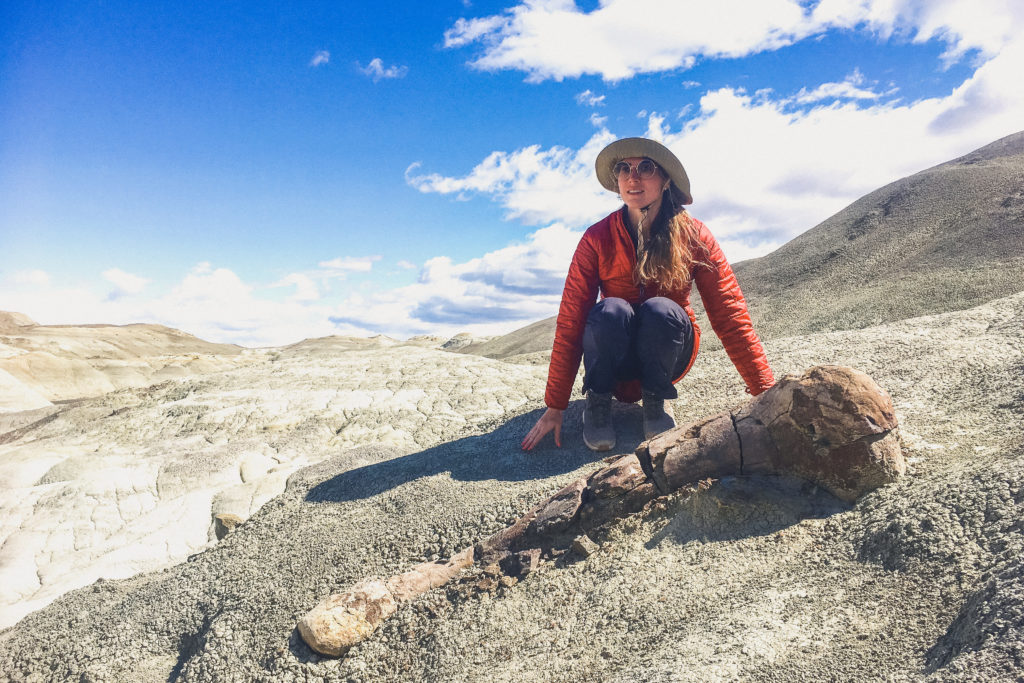 woman stands next to dinosaur femur fossil