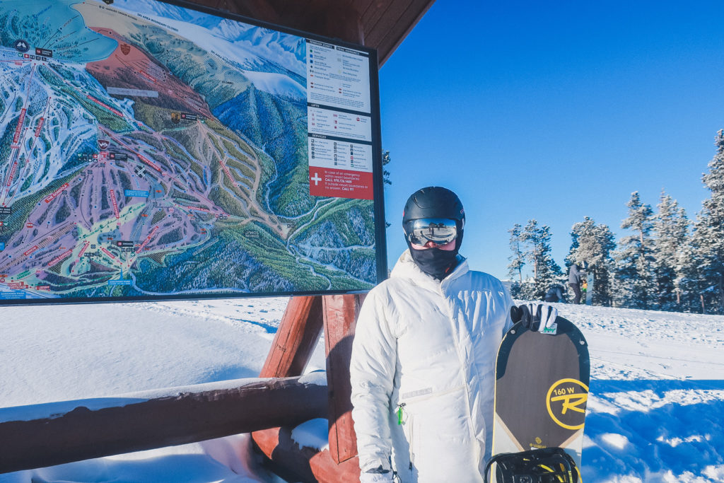 man with snowboard stands in front of Winter Park trail map